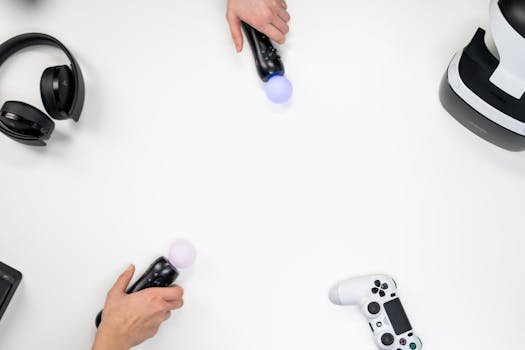 Top view of hands with gaming controllers, headphones, and VR headset on a white background.